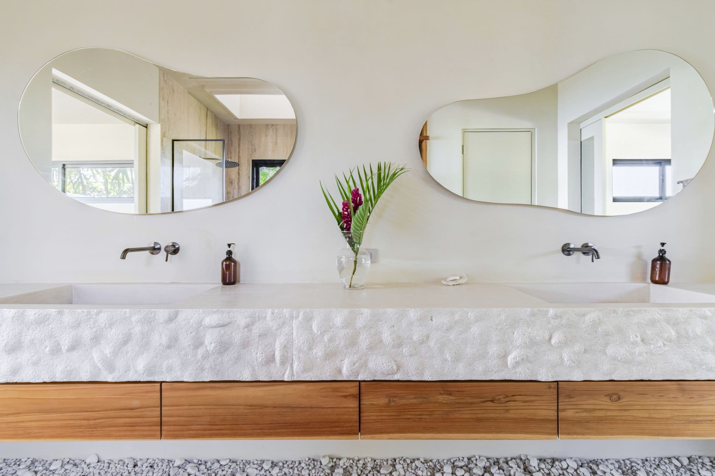Sculpted white double vanity with two organic-shaped mirrors and wall-mounted faucets