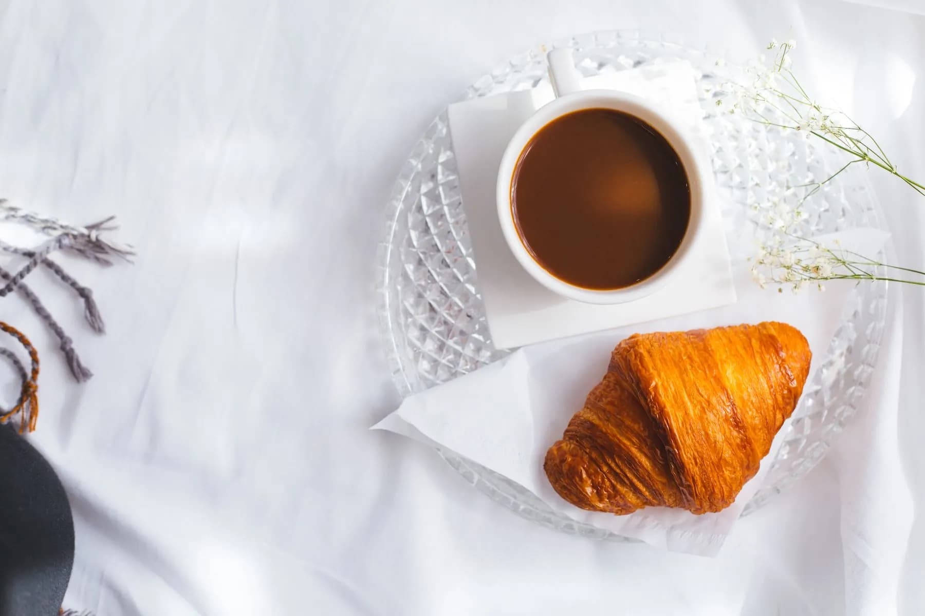 Illustrative cuisine photo: A croissant and a cup of coffee on a glass plate over white linen.