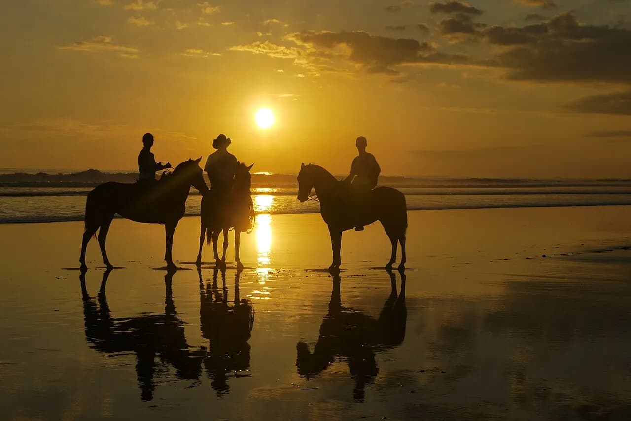 Riders on horseback silhouetted against a golden sunset at Playa Esterillos