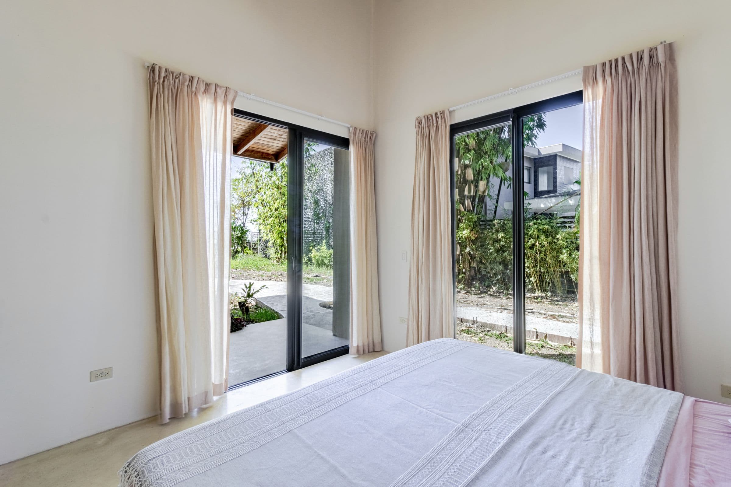 King bed facing floor-to-ceiling glass doors that open onto a tropical garden path