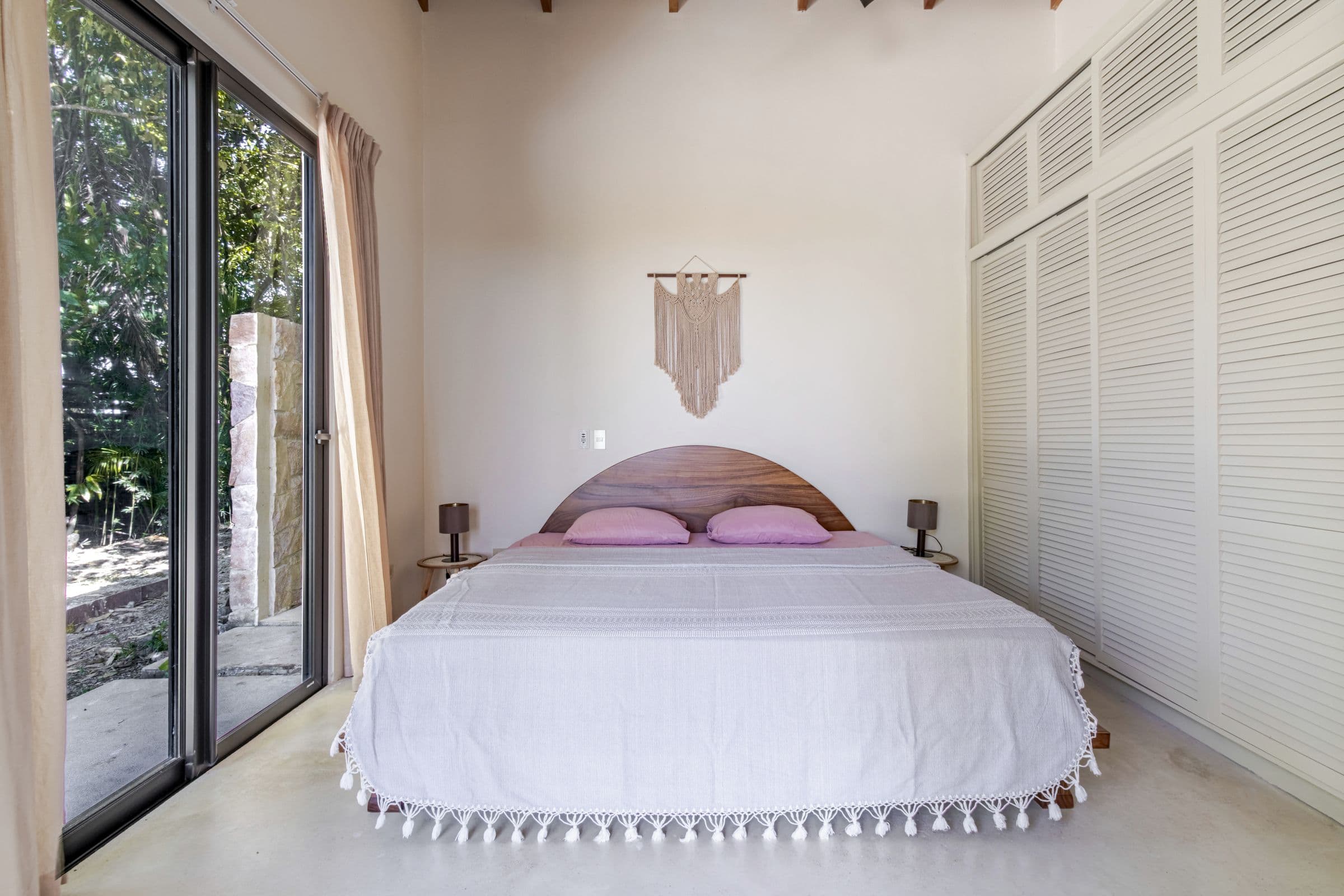 King bedroom with an arched wooden headboard, macramé wall hanging and sliding glass doors to the garden