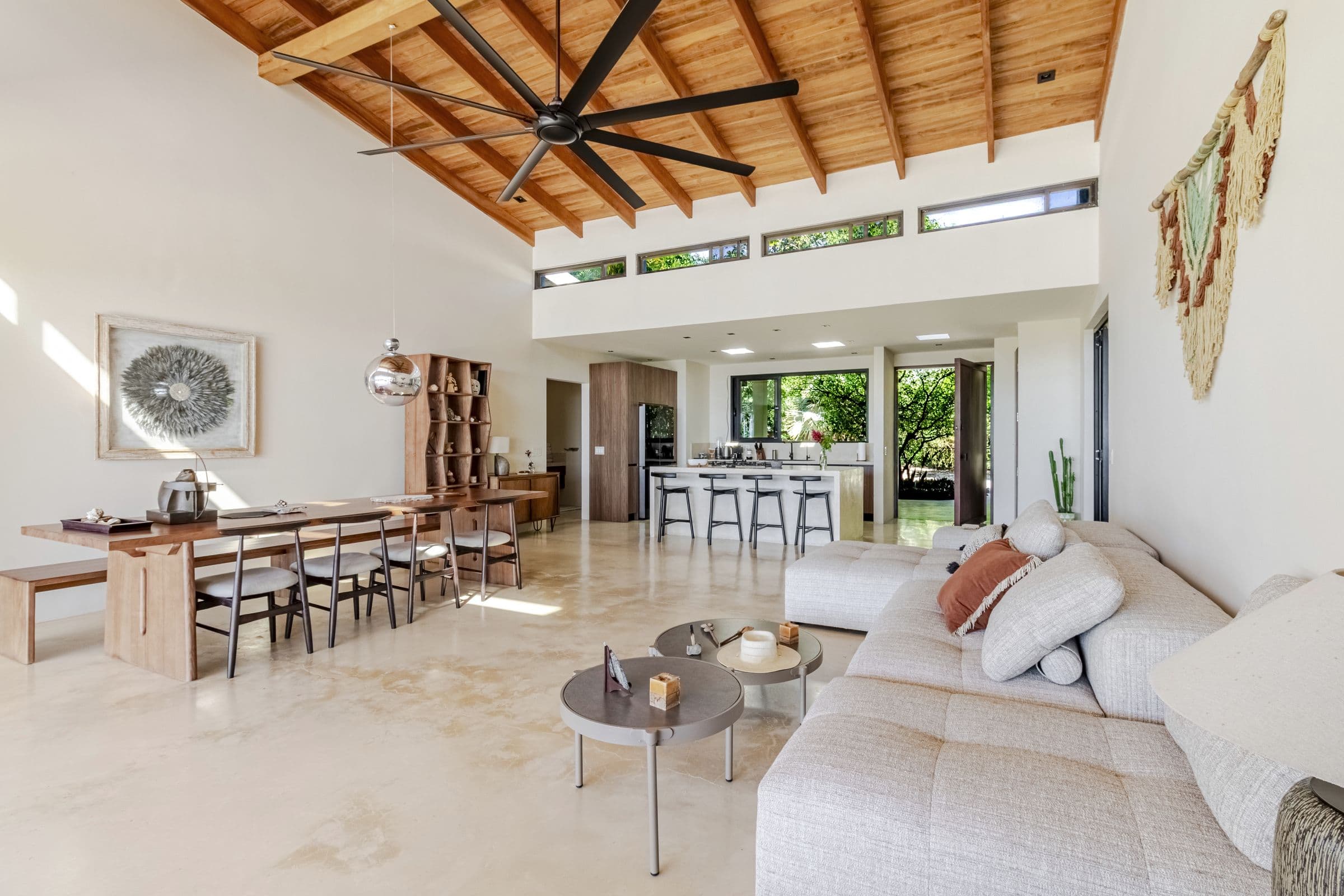 Open-plan great room with a vaulted wood ceiling, sectional sofa, long dining table and kitchen island