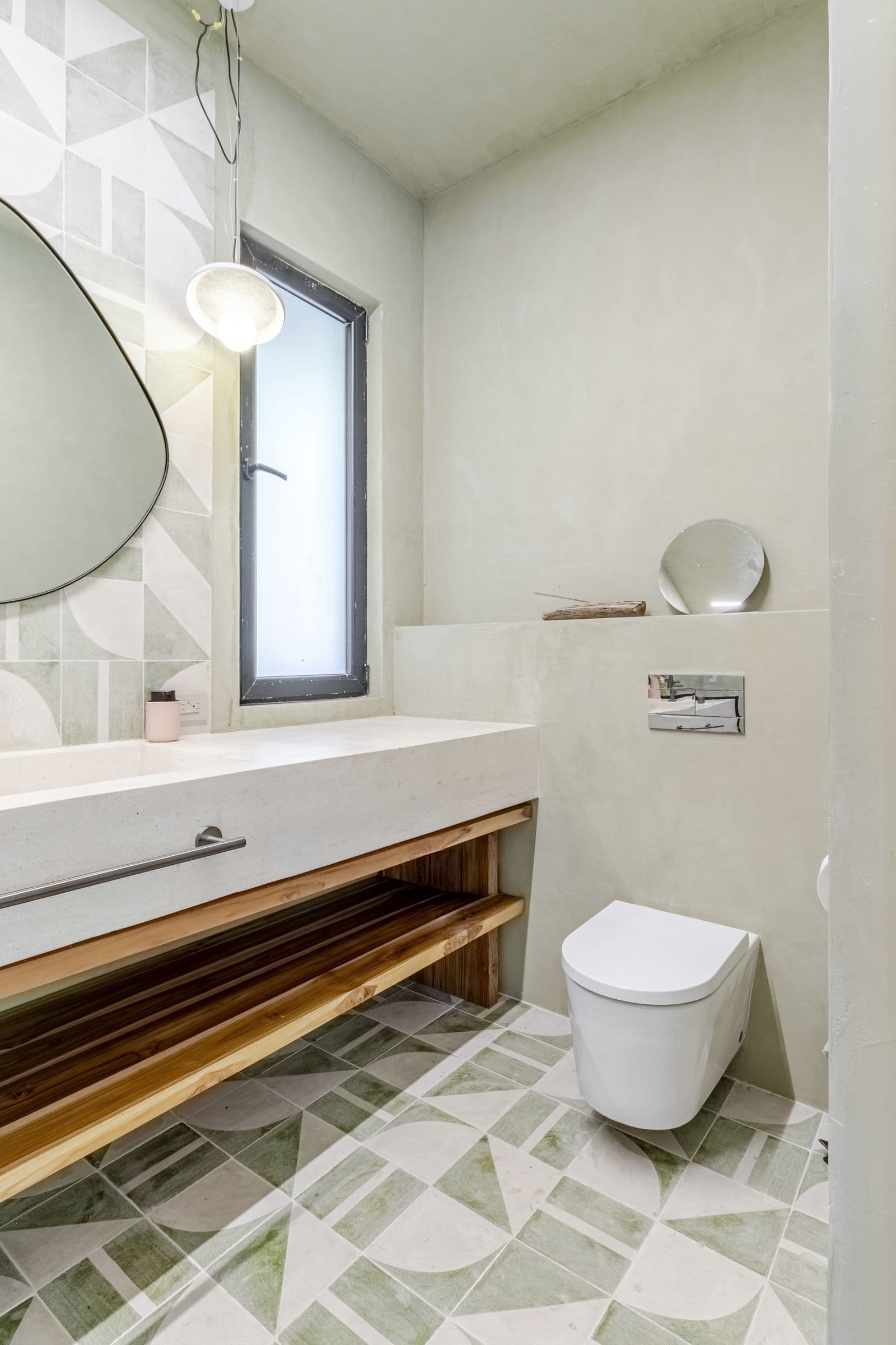 Bathroom with a patterned green tile floor, a long basin counter and a wall-hung toilet