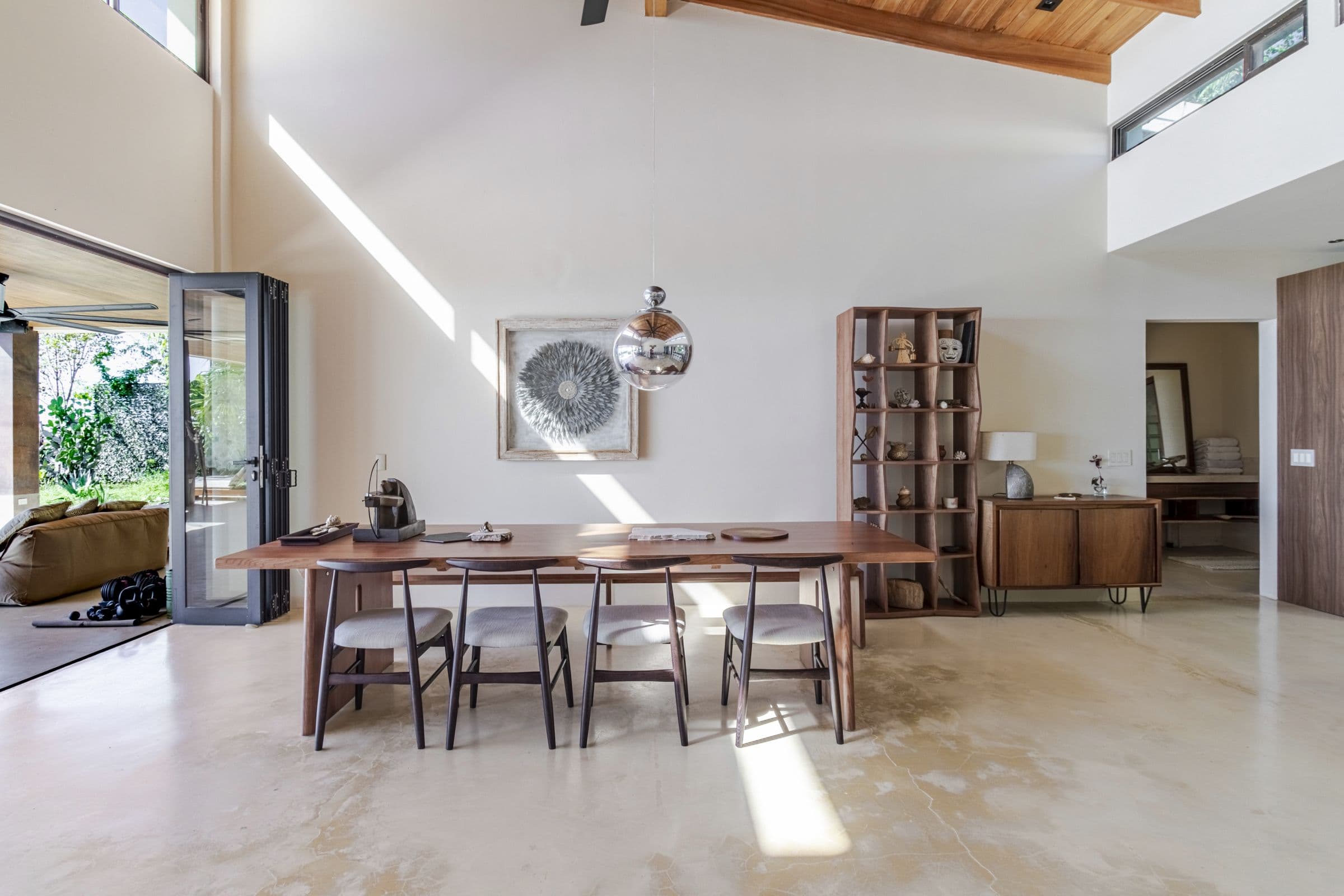 Long wooden dining table under a glass pendant light and clerestory windows