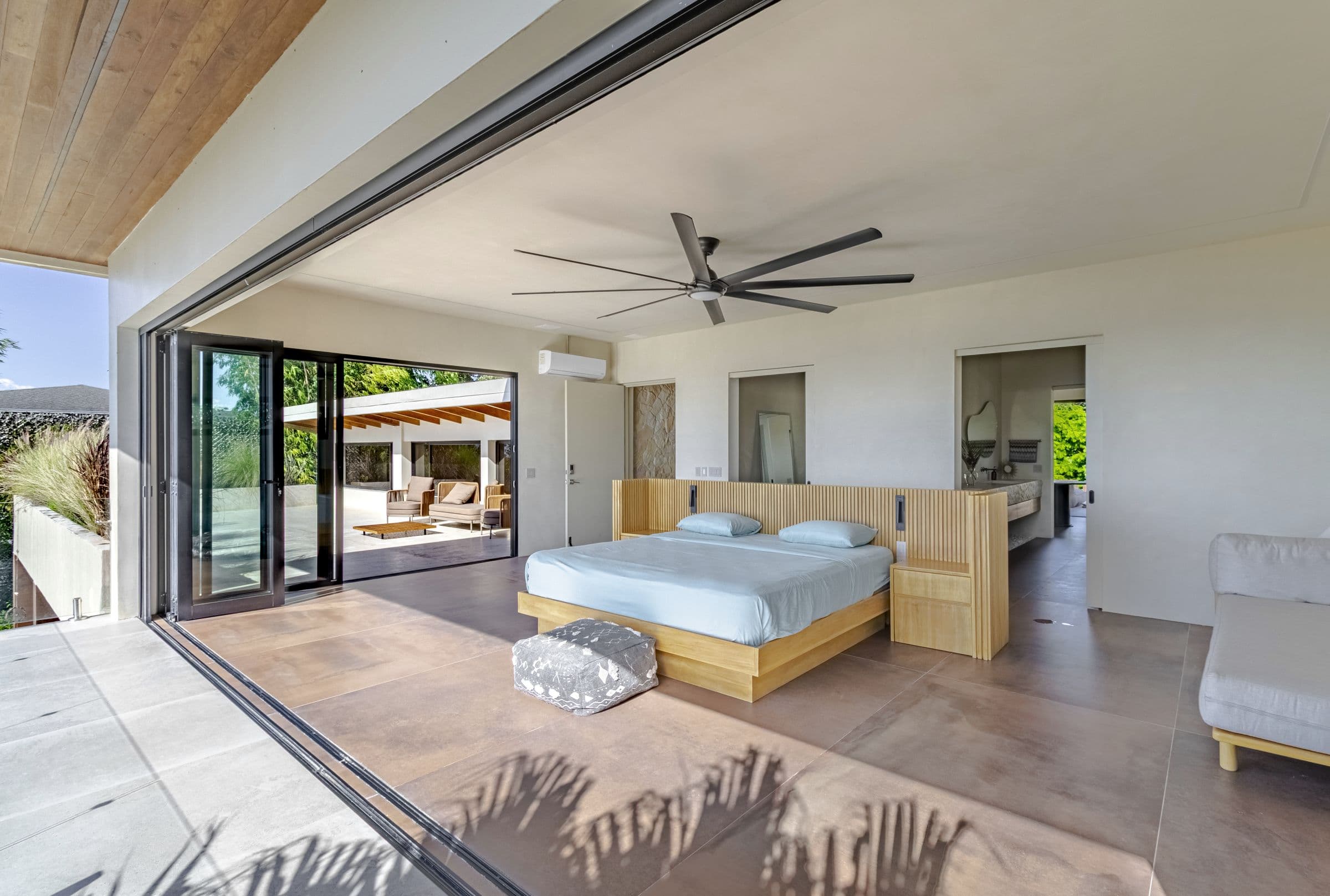 Upper-floor king bedroom with its glass walls folded fully open to the terrace