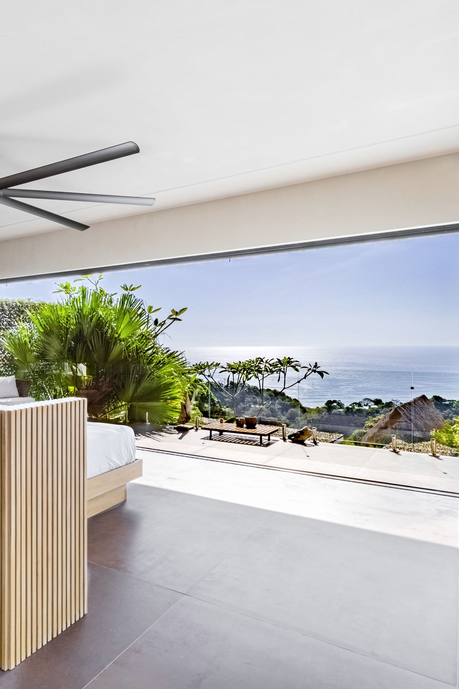 Upper-floor king bedroom with folding glass walls framing an ocean and jungle view