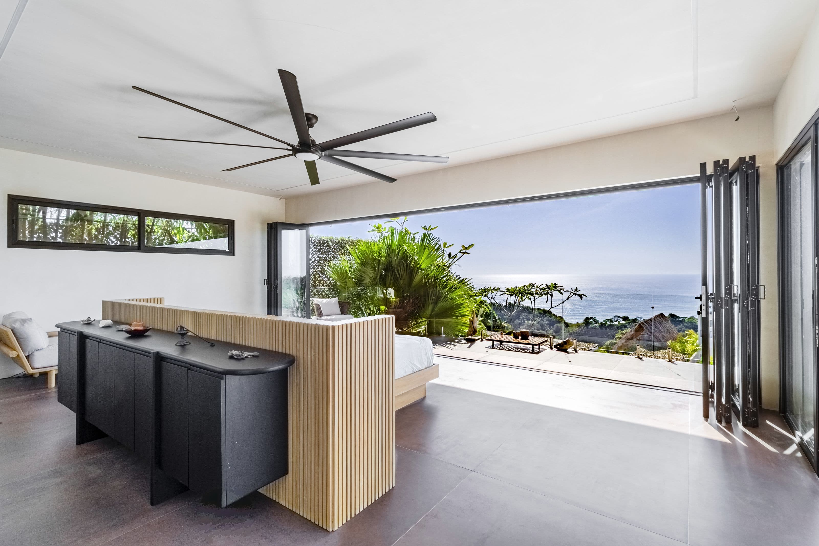 Upper-floor king bedroom with folding glass walls framing an ocean and jungle view