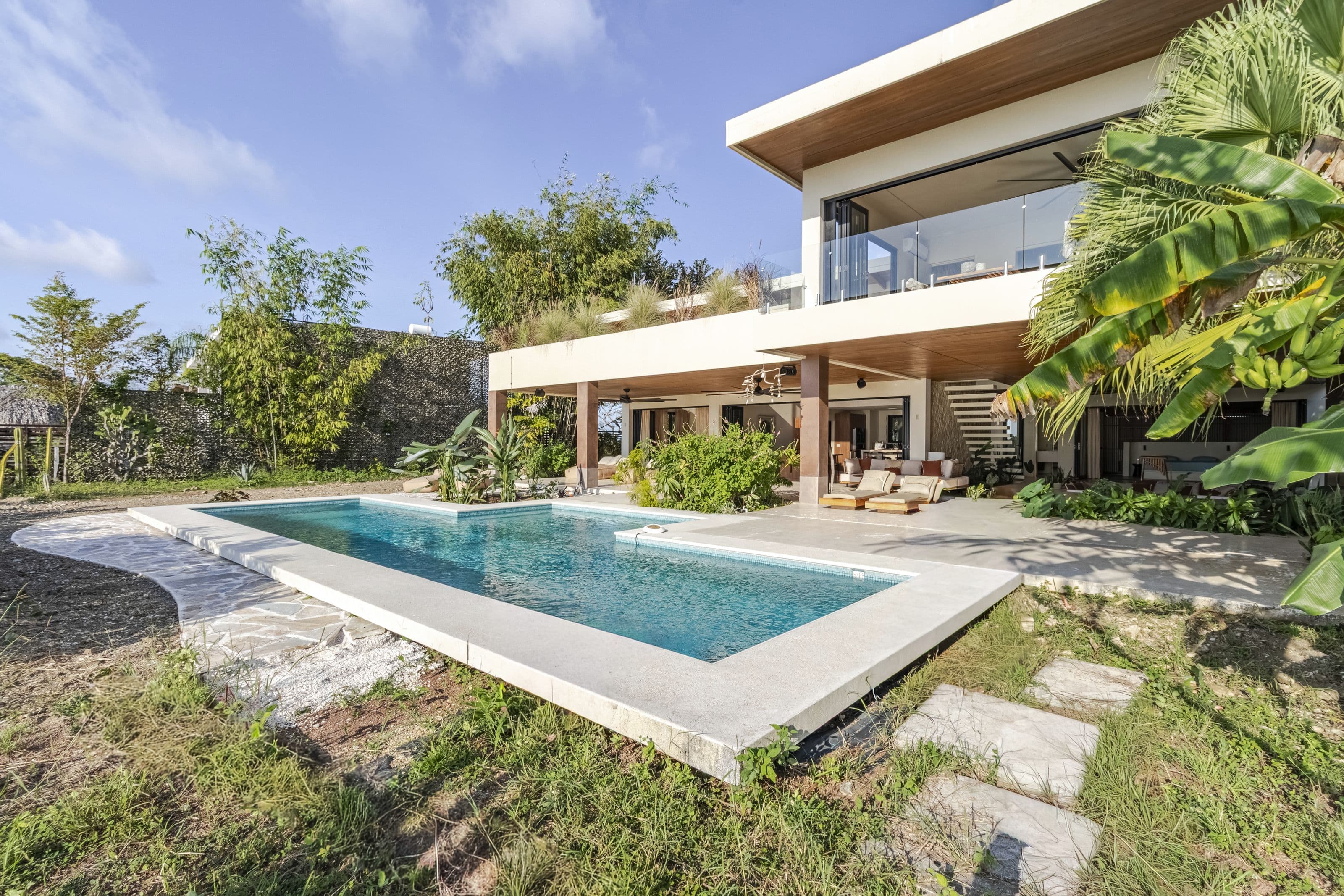 Swimming pool and lawn with the two-story villa and jungle garden behind