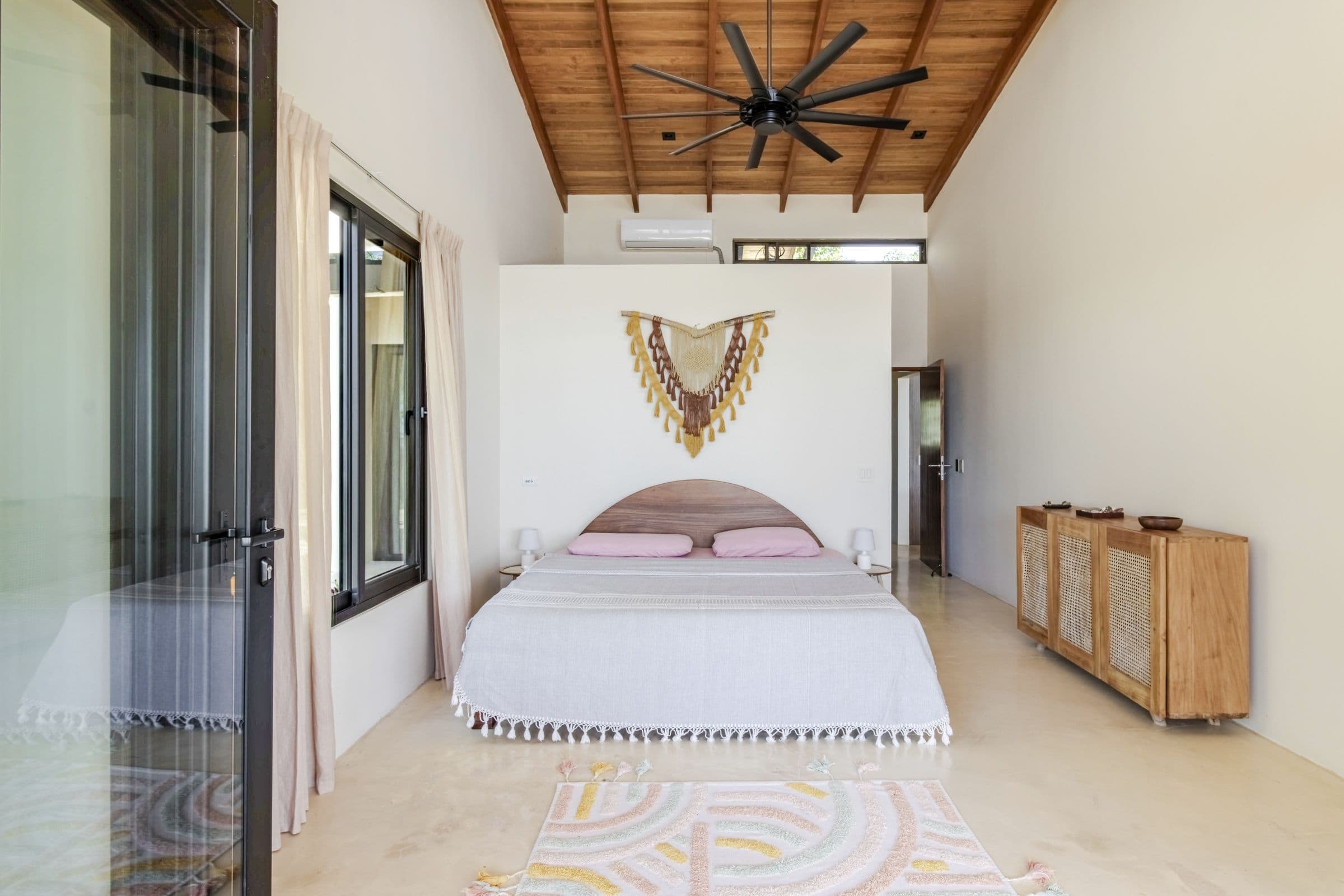 King bedroom with a vaulted timber ceiling, ceiling fan, arched wooden headboard and patterned rug