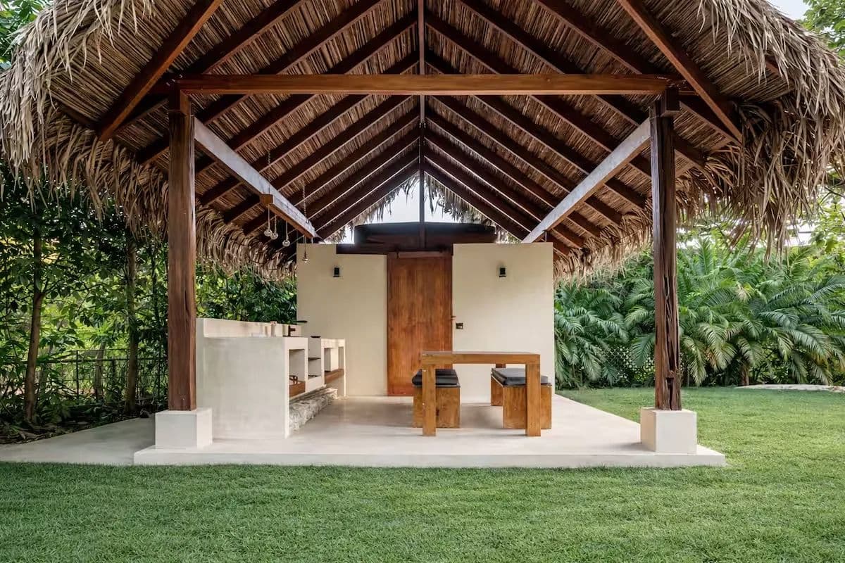 Thatched rancho on the lawn with a barbecue counter and a wooden dining table