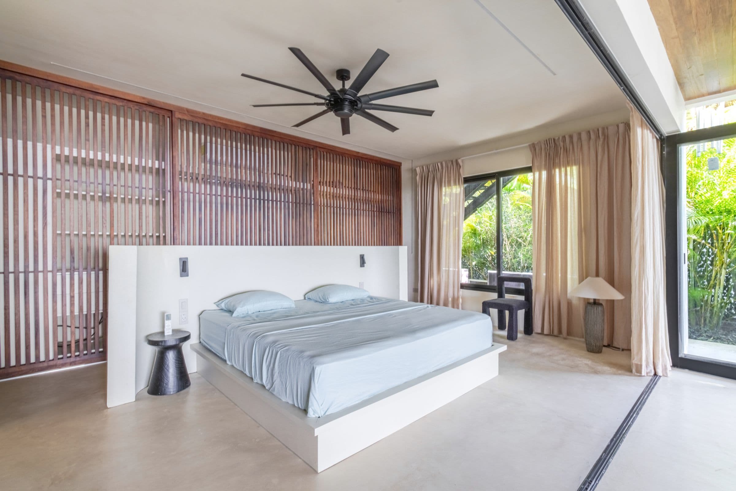 King bedroom with a slatted timber feature wall, sheer curtains and garden views