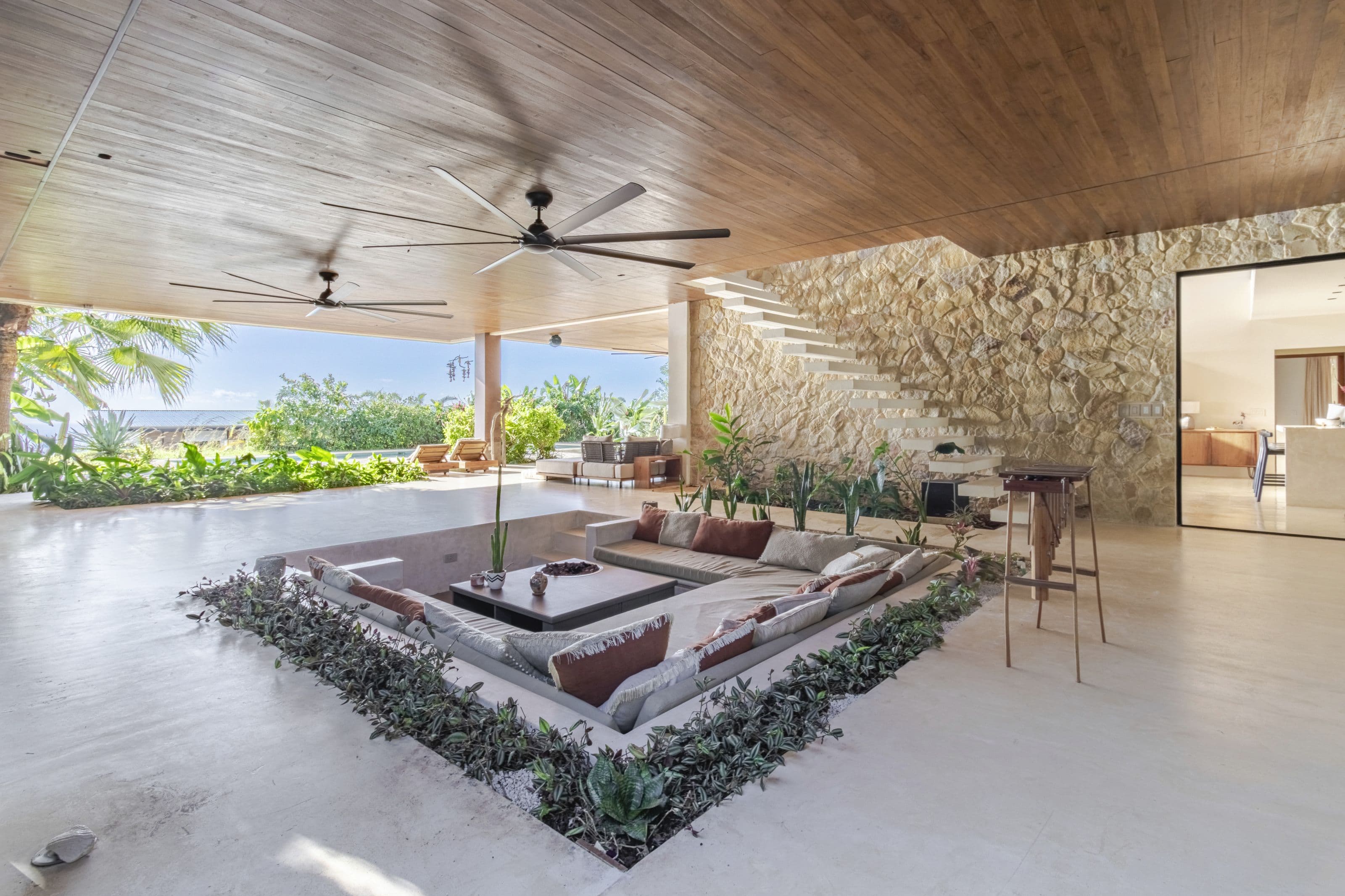 Sunken conversation lounge ringed with plants under a warm timber ceiling