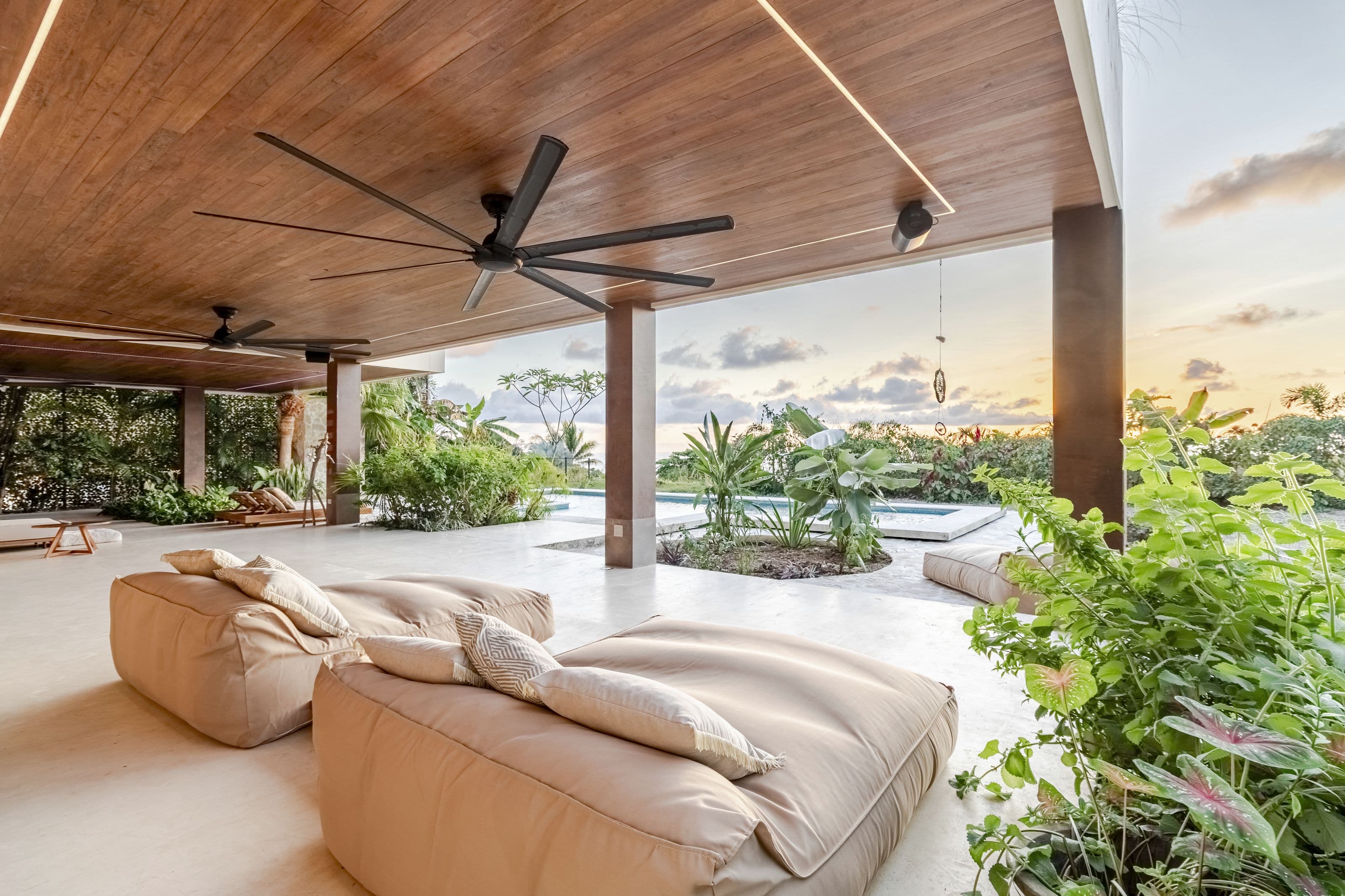 Cushioned loungers on the covered terrace with the pool and garden beyond
